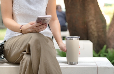 벤치에 앉아서 컵을 내려놓고 휴대폰을 보고 있는 사람 사진